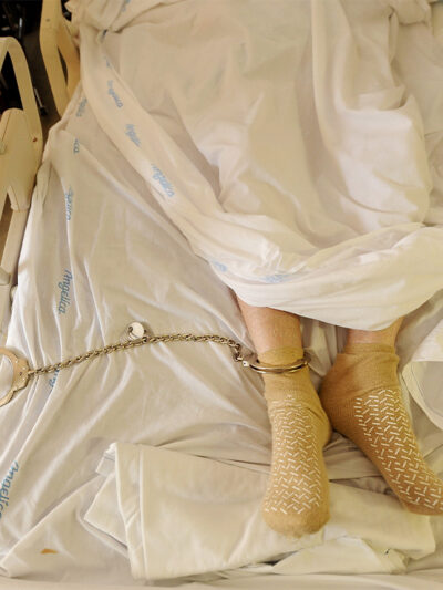 A prisoner lying in a hospital bed with one leg shackled to the bed rail in California medical facility.