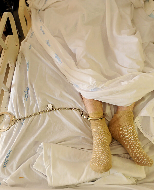 A prisoner lying in a hospital bed with one leg shackled to the bed rail in California medical facility.