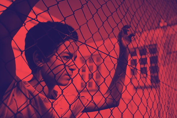 Photo of student looking through a chain link fence. Photo has been recolored to have values of red and navy blue only.