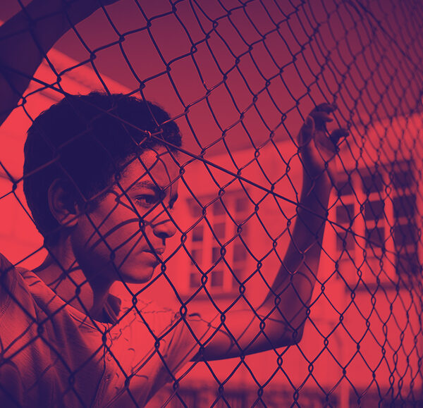Photo of student looking through a chain link fence. Photo has been recolored to have values of red and navy blue only.