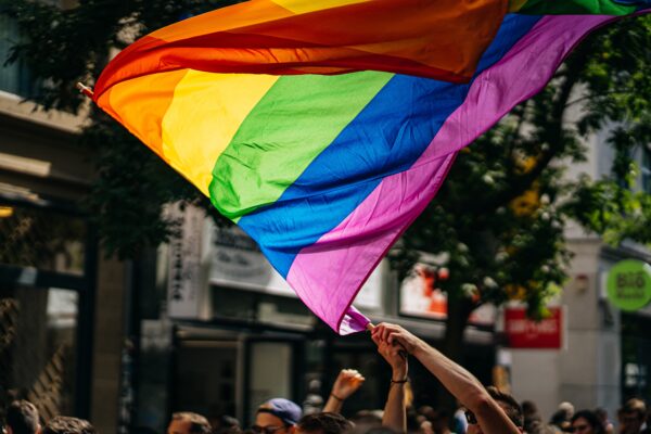A person's arms waving a Pride flag at a march in a city.