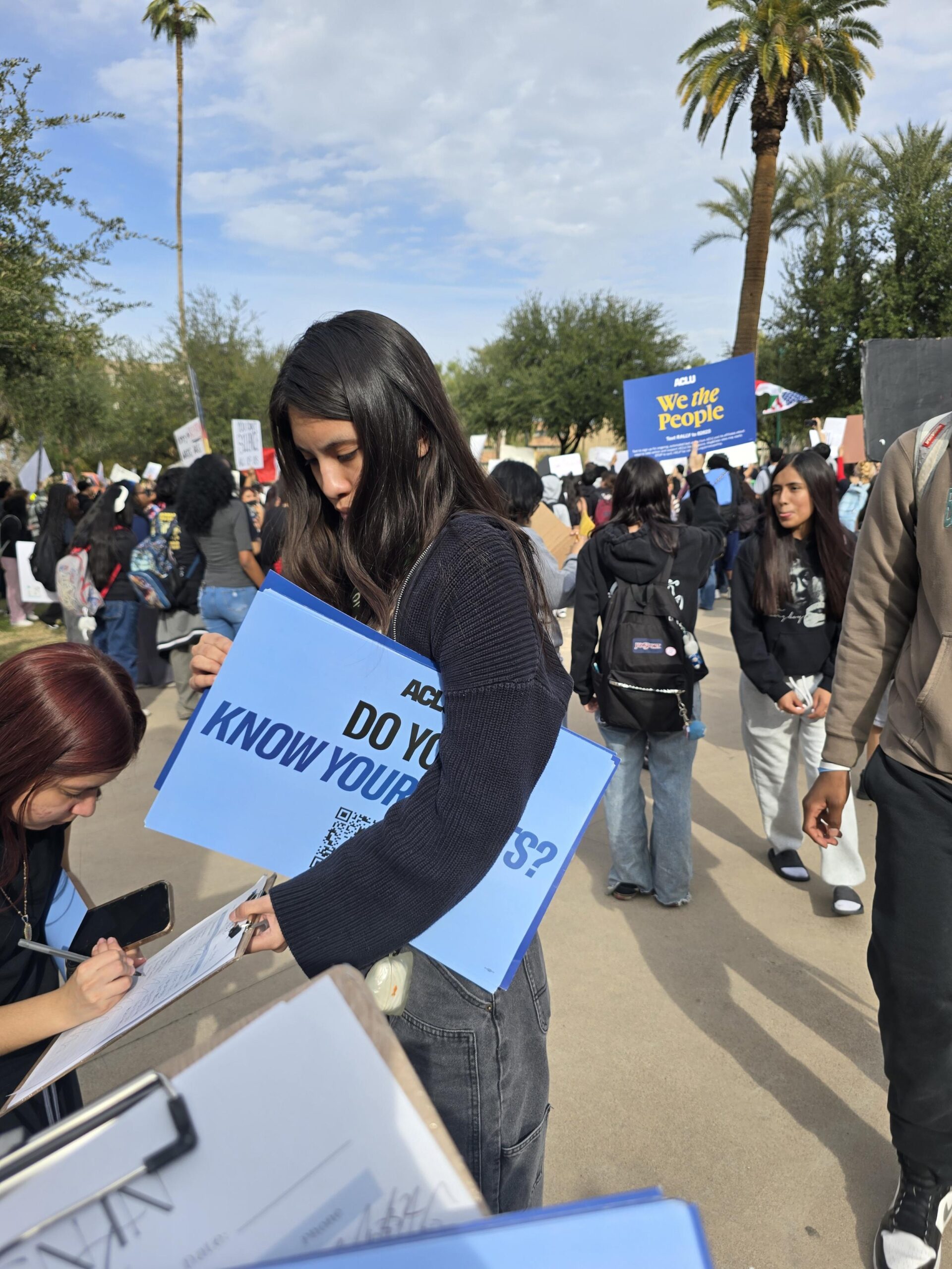 A young woman with long black hair signing up volunteers at a protest.