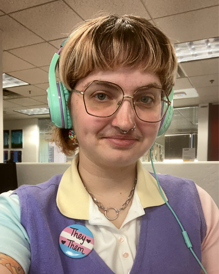 Person with blonde bangs wearing teal headphones, glasses, a yellow polo under a purple vest wearing a they/them button.