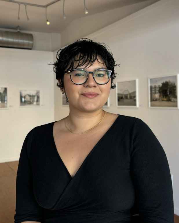 A woman with short black hair and glasses wearing a black blouse.