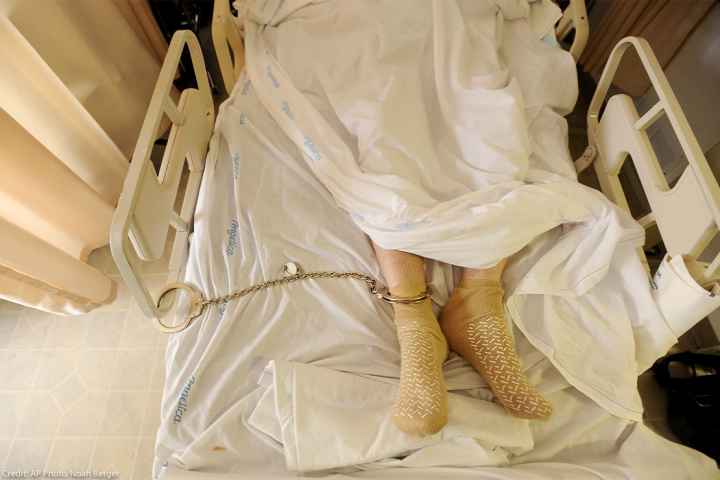 A prisoner lying in a hospital bed with one leg shackled to the bed rail in California medical facility.